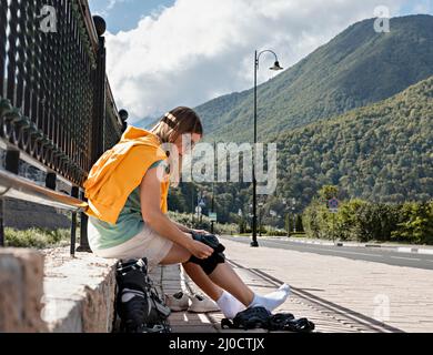 Giovane donna in felpa con cappuccio gialla che mette su attrezzature di protezione prima di pattinare sul terrapieno stile di vita attivo, attività all'aperto, roller skat Foto Stock