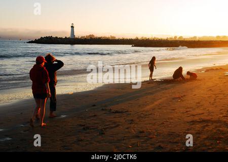 La gente cammina e gioca su una spiaggia mentre il sole scende Foto Stock