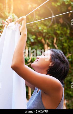 Questa lavanderia si asciugherà in un istante. Scatto di una giovane donna che appende la lavanderia sulla linea di lavaggio. Foto Stock