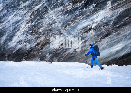 Turista in costume blu con zaino vicino grotta di ghiaccio parete testurizzata al ghiacciaio nel bel paesaggio della valle di montagna coperta di neve in Almaty, Ka Foto Stock