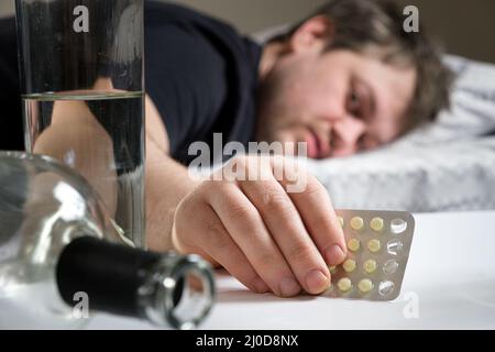 Un uomo si trova su un letto dopo una festa di alcol, tenendo in mano le pillole di hangover Foto Stock