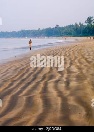 Sindhudurg, India - 20 dicembre 2021 : Coppia non identificata che fa jogging sulla spiaggia durante le ore del mattino. Bella texture di sabbia di mare. Verticale o po Foto Stock