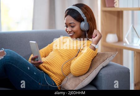 Home è il mio posto felice. Scatto di una ragazza attraente indossando le cuffie mentre usando il suo cellulare. Foto Stock