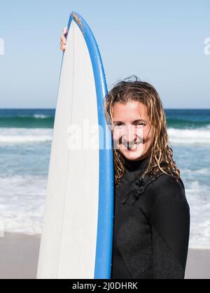 Ritratto femminile di surfista caucasico che tiene la sua tavola da surf indossando la muta invernale Foto Stock