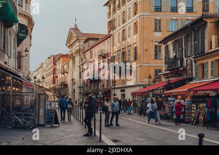 Nizza, Francia - 10 marzo 2022: Le persone passeggiando accanto ai negozi di souvenir a Cours Saleya, la più grande zona pedonale della Vieux Nice (Città Vecchia) per cui è meglio conosciuta Foto Stock