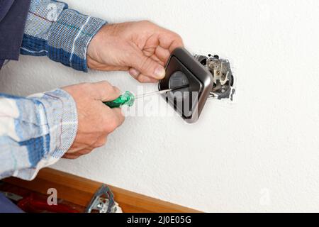 L'operatore con il cacciavite in mano sta fissando una presa elettrica Foto Stock