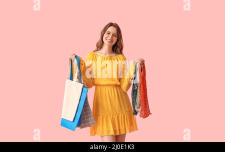 Bella giovane donna con borse ecologiche su sfondo rosa Foto Stock