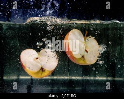 mele a fette che cadono in acqua su sfondo scuro. Vista subacquea. Cucina, vegetariana, cucina a casa concetto Foto Stock