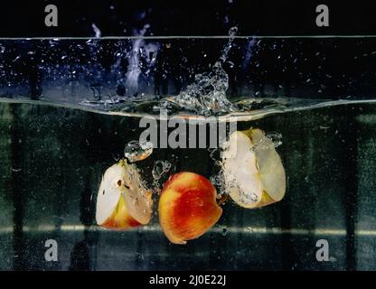 mele a fette che cadono in acqua su sfondo scuro. Vista subacquea. Cucina, vegetariana, cucina a casa concetto Foto Stock