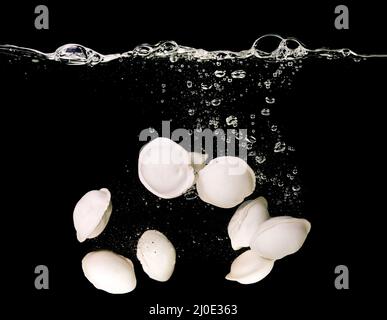 Gnocchi (ravioli) sott'acqua in acqua bollente sott'acqua in padella su sfondo scuro. Cucina italiana, cinese Foto Stock