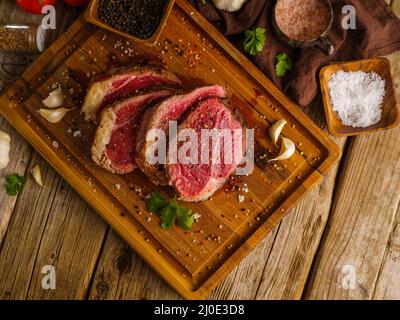 Pezzi crudi carne, maiale, vitello, manzo cosparsi di spezie su sfondo di legno. Vista ad angolo basso. Cucina bistecche di carne. Ristorante, hotel, cucina casalinga Foto Stock