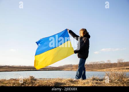 Bandiera Ucraina giallo-blu contro il cielo nelle mani di una giovane donna. Simbolo nazionale di libertà e indipendenza. Sostenere l'Ucraina, orgoglio e patr Foto Stock