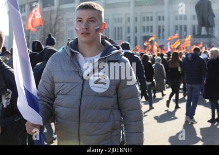 Mosca, Russia. 18th Mar 2022. 18 marzo 2022, Russia, Moskau: Le persone hanno bandiere ai margini di un concerto che segna l'ottavo anniversario dell'annessione della penisola del Mar Nero di Crimea il 18 marzo 2014, con un giovane che porta un adesivo con una grande 'Z' e le parole 'non lasceremo il nostro popolo alle spalle' in russo. Credit: dpa Picture Alliance/Alamy Live News Foto Stock