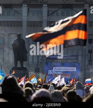 Mosca, Russia. 18th Mar 2022. 18 marzo 2022, Russia, Moskau: Le persone hanno bandiere nei colori del nastro di San Giorgio, un'insegna militare russa, per esprimere il loro sostegno al corso del governo del Presidente Putin, al margine di un concerto per celebrare l'ottavo anniversario dell'annessione della penisola del Mar Nero di Crimea, 18 marzo 2014. Sullo sfondo sorge un monumento a Lenin. Credit: dpa Picture Alliance/Alamy Live News Foto Stock