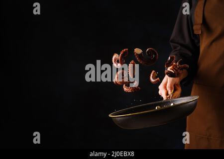 Uno chef professionista prepara i polpi in una padella su sfondo nero. Levitazione. Cucina di pesce, cibo vegetariano sano. È gratuito Foto Stock