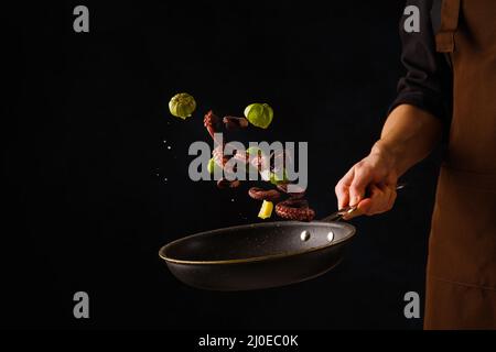 Frutti di mare. Uno chef professionista prepara frutti di mare - pezzi di polpo con limone in una padella su sfondo nero. Levitazione. Ristorante, hotel. R Foto Stock