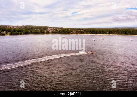 Piccola barca a motore veloce che accelera sulla superficie dell'acqua della baia di Jervis della costa del pacifico Australiana - mare aereo. Foto Stock