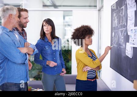 Let me sketch it out for you. Shot of a team of coworkers planning a storyboard on a blackboard. Foto Stock