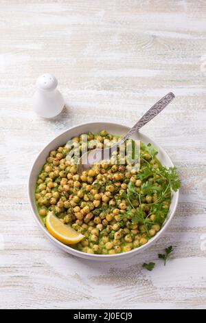 Ceci stufati in salsa verde con prezzemolo e limone su sfondo bianco in legno, stile rustico, vista dall'alto. Delizioso cibo sano fatto in casa Foto Stock