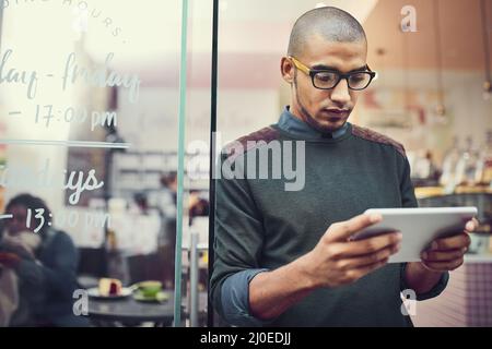 Tenere d'occhio la sua concorrenza. Scatto di un uomo che usa il suo tablet digitale mentre si trova all'ingresso di un bar. Foto Stock