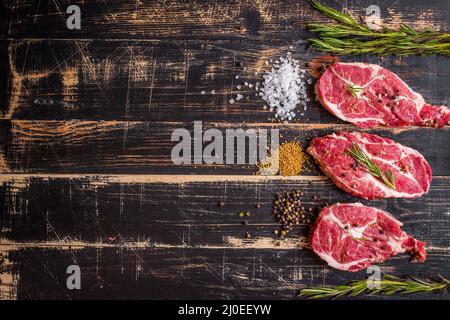 Carne cruda bistecca su scuro dello sfondo di legno pronti per la tostatura Foto Stock