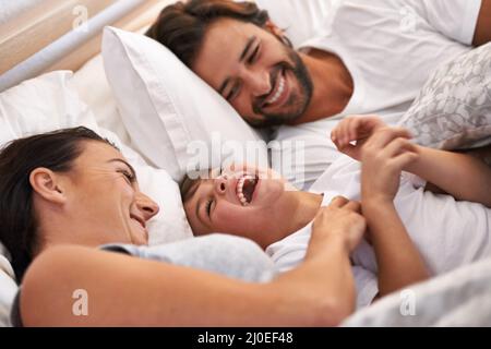 Vuole sempre essere vicino a mummia e papà. Scatto corto di una giovane famiglia a letto insieme. Foto Stock