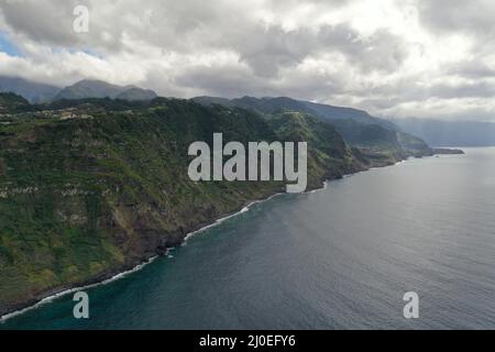 Vista aerea delle spettacolari scogliere settentrionali di Madeira sotto pesanti nuvole vicino a São Vicente, mostrando ripide pareti vulcaniche che incontrano il vasto Oceano Atlantico Foto Stock