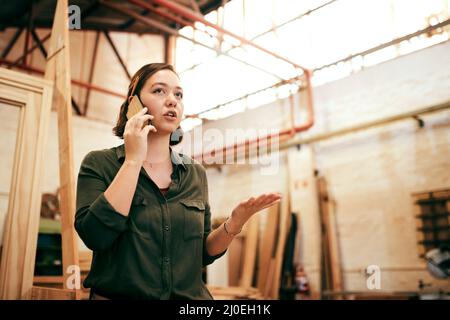 Im sempre gettin nuovi ordini. Shot di una carpentiere femmina che parla sul suo cellulare mentre si trova in piedi nella sua officina. Foto Stock