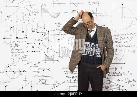 Matematico caucasico di mezza età che spiega le equazioni matematiche su una parete bianca Foto Stock