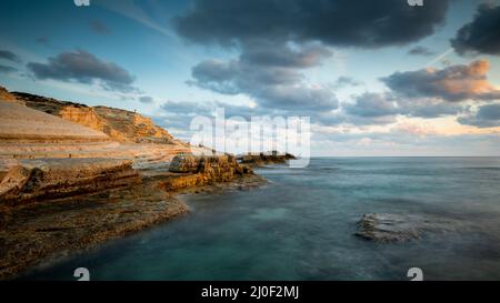 Litorale roccioso con un tramonto spettacolare e bellissimo nella zona costiera delle grotte marine di Paphos, CYP Foto Stock