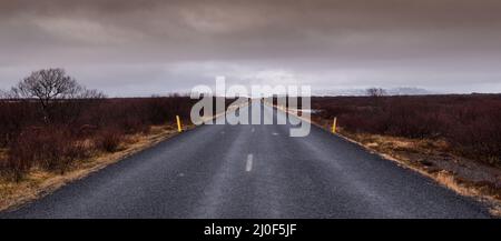 Autostrada strada dritta che porta alle montagne innevate in Islanda Foto Stock