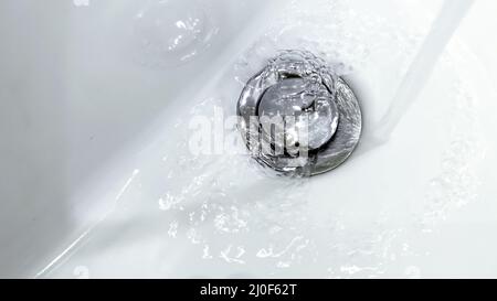 L'acqua che cade da un rubinetto in un lavandino in ceramica bianca Foto Stock