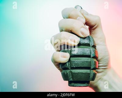 Una foto in primo piano di una mano strizza una granata militare verde su uno sfondo multicolore. Foto Stock