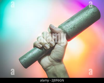 La mano tiene una granata sportiva in ferro su uno sfondo multicolore. Foto di primo piano Foto Stock