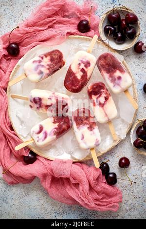 Panna fresca e ciliegia pop-icles fatti in casa posto su piastra di ceramica bianca con frutta e tessuto Foto Stock