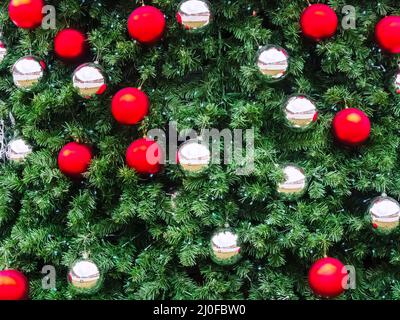 Palle di Natale rosse e argentate pendono su rami artificiali di abete. Texture di sfondo Foto Stock