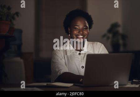 Guardando l'orologio im guardando il mio saldo banca salire. Ritratto di una giovane donna d'affari che utilizza un computer portatile durante una notte tarda al lavoro. Foto Stock