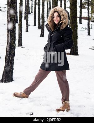 Giovane ragazza felice e bella adolescente vestita di abbigliamento invernale in piedi sulla neve e sorridente. Foto Stock