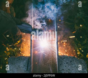 L'uomo che lavora saldatore brucia attraverso un foro di elettrodo in un canale di acciaio la sera Foto Stock