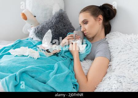 Un giovane adolescente beve il tè caldo con le erbe mentre si trova sul suo letto sotto le coperte. Foto Stock