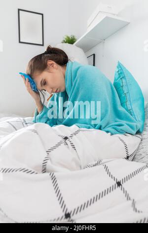 L'adolescente mette compresse fredde sulla sua testa per ridurre l'alta temperatura. Foto Stock