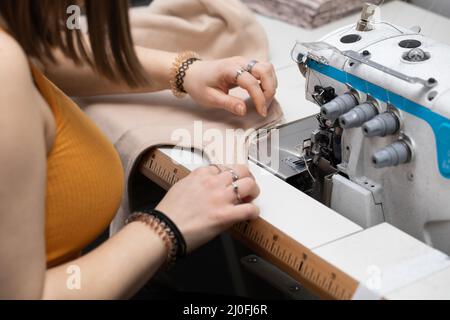 Un adolescente cucia un abito marrone su una macchina da cucire chiamata overlock. Foto Stock