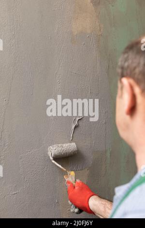 In bagno, un lavoratore di costruzione generale applica l'isolamento di umidità usando un rullo. Foto Stock