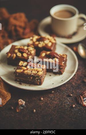 Torta al cioccolato con glassa al caramello, noci pecan e caffè caldo, su sfondo rustico. Appena sfornato Foto Stock