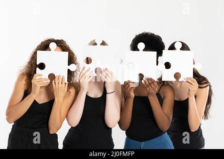 Quattro ragazze stanno tenendo puzzle nelle loro mani, coprendo il loro volto per diventare anonime e dimostrare che le differenze si collegano, Foto Stock