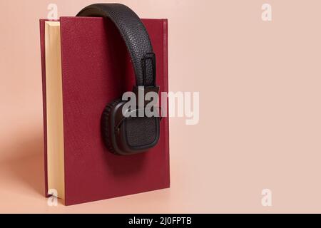 Audiolibro. Le cuffie sono posizionate su un libro spesso su uno sfondo colorato Foto Stock