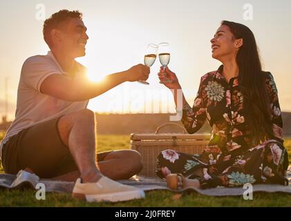 Ti amo per tutto quello che sei. Scatto di una giovane coppia che fa un brindisi mentre su un picnic ad un lago. Foto Stock