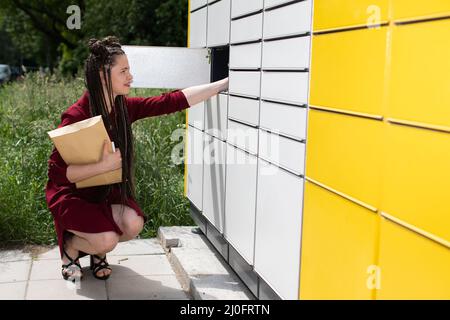 Un adolescente prende un pacco da un armadietto del pacco. Aprire la mailbox. La ragazza tira tutti i pacchi dalla cassetta delle lettere. Foto Stock