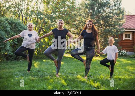 Femmine beatissful di quattro generazioni di una famiglia in piedi su una gamba che tiene le mani che si riscaldano su prato pieno di verde. Trascorrere del tempo Foto Stock