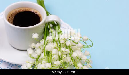 Una tazza di caffè nero su un piattino e un bouquet di Lily della valle fiori su uno sfondo azzurro Foto Stock